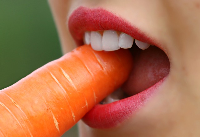 Kobieta z białymi zębami gryzie marchewkę